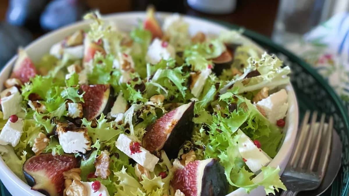Salade de chicorée frisée, figues, chèvre et noix dans une assiette blanche