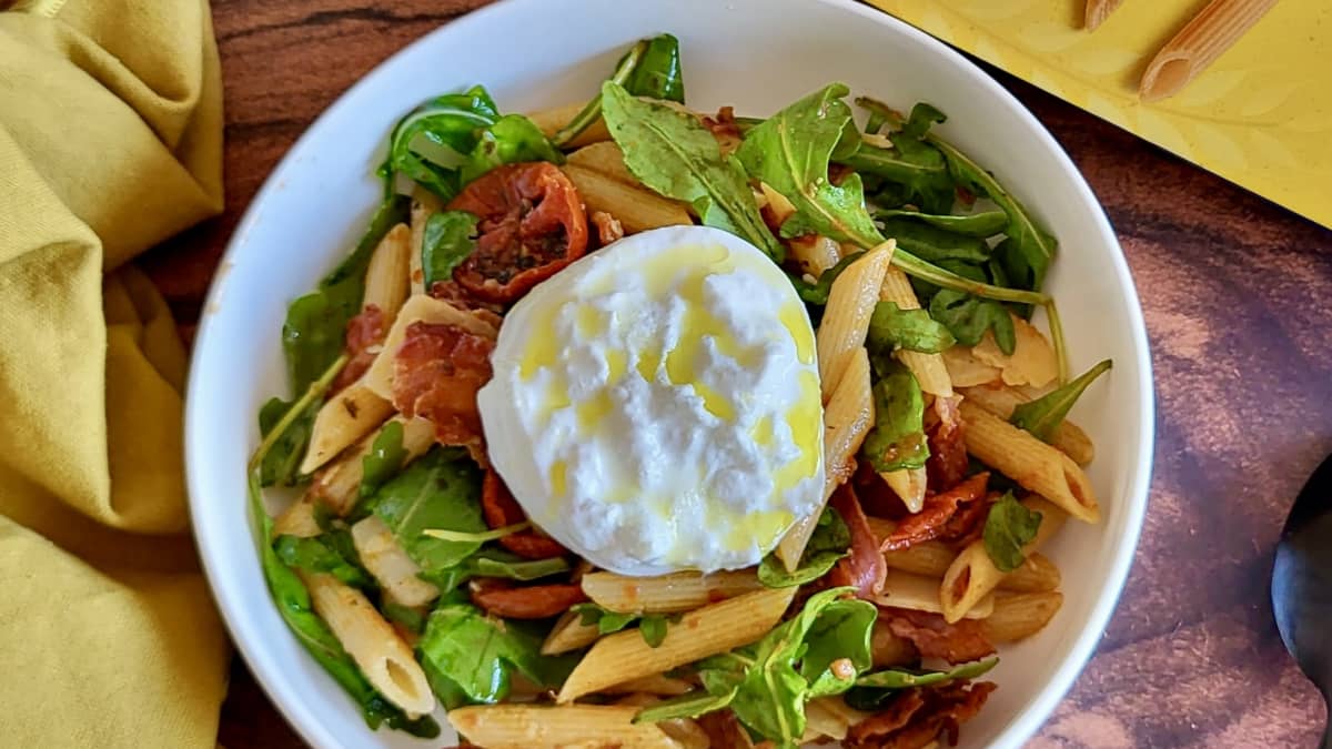 Assiette de penne pesto rosso, bacon croustillant et boule de burrata