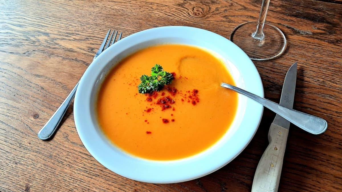 Assiette de soupe de patates douces et poivrons et couverts posés sur une table en bois