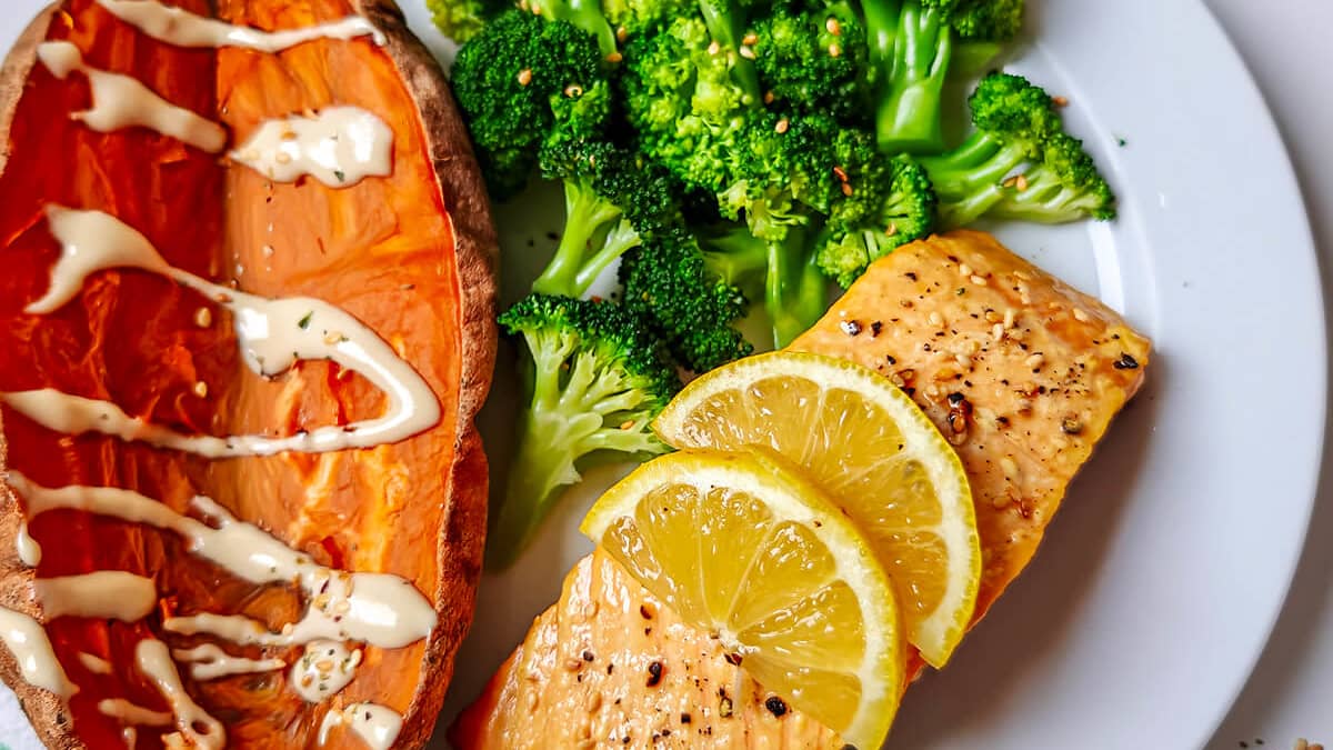Gros plan sur une assiette blanche dressée avec saumon, brocolis et patate douce