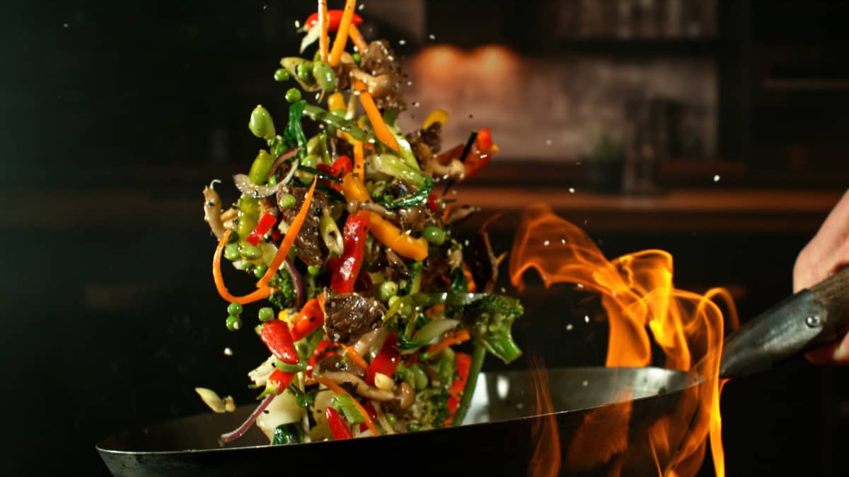 Wok avec des ingrédients qui volent dans les airs et des flammes.