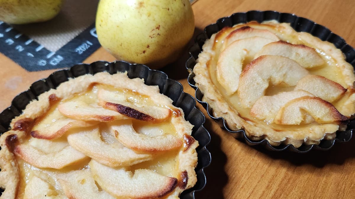 2 tartelettes aux poires dans leurs moules, sur une table en bois avec une poire entière