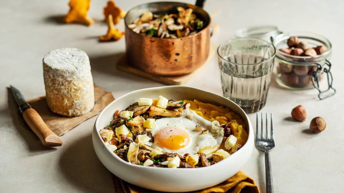 Assiette de purée de courge, champignons en persillade et oeuf au plat, sur une table avec les ingrédients