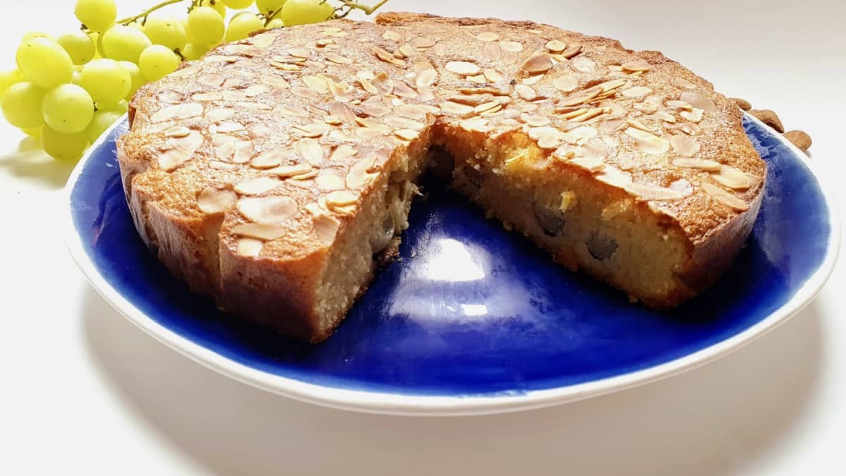 Gâteau moelleux à l'amande et aux raisins, sans farine, entamé, sur un plat de service bleu