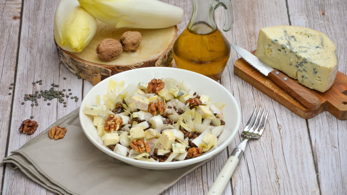 Assiette de salade de lentilles aux endives posée sur une table avec les ingrédients