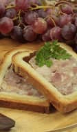 2 tranches de pâté en croûte posées sur un plateau en bois, avec couteau, raisins, tomate et cornichons