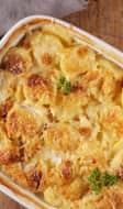 Plat de gratin dauphinois posé sur une table en bois avec pommes de terre, épluche-légume et couverts de service