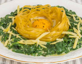Oeuf dans un nid de pâtes sur un lit d'épinards