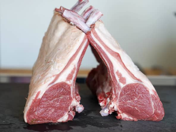 Carrés d'agneau parés et manchonnés sur planche noire.