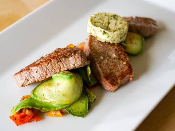 Beurre d'estragon sur noisettes d'agneau et tagliatelles de courgette sur assiette blanche