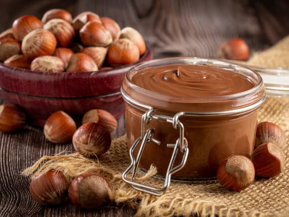 Pot en verre de crème de noisettes entouré de noisettes