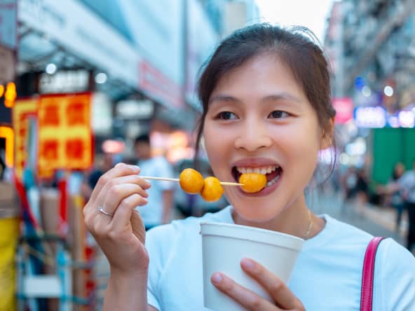 Jeune femme asiatique mangeant des fish balls dans les rues de Hong Kong