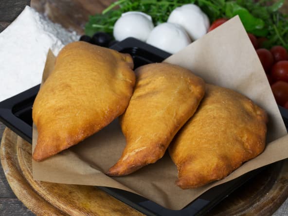 Panzerotti posés sur papier sulfurisé et assiette noire.