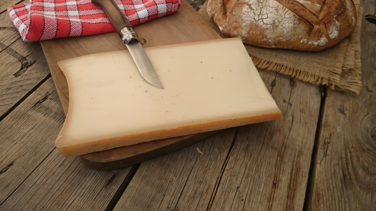 Morceau de beaufort tranché avec couteau, pain et serviette sur une table en bois