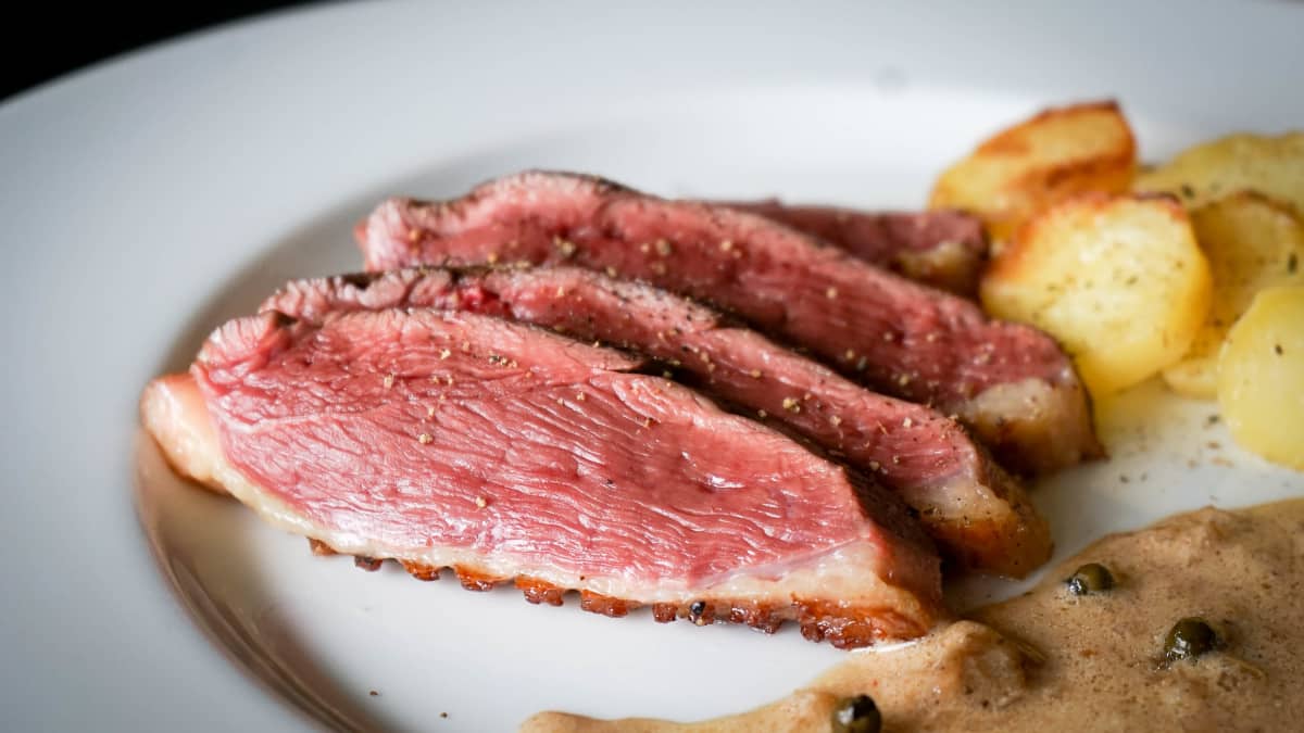 Aiguillettes de magret de canard au poivre vert sur assiette.