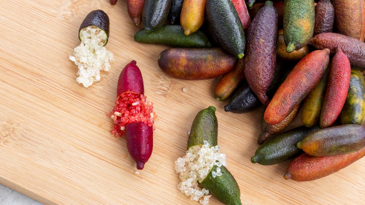Citrons caviar de 3 couleurs différentes, coupés en deux et entiers, posés sur une planche en bois
