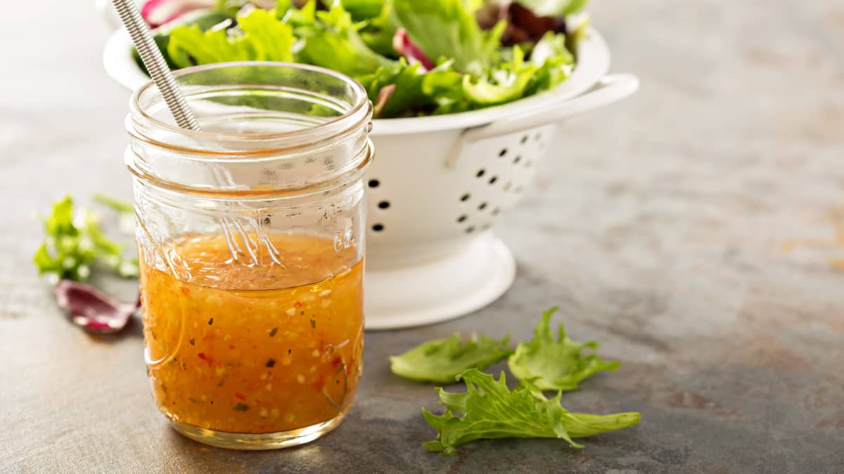 Pot de sauce vinaigrette et salade dans une passoire blanche