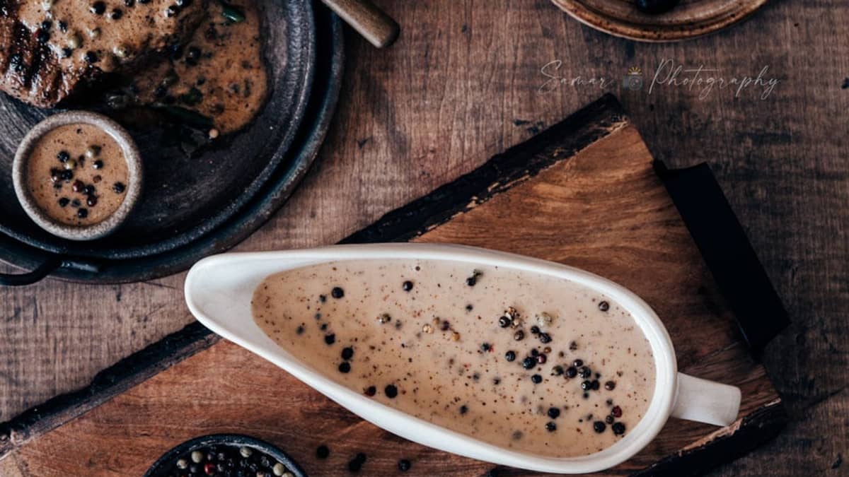 Sauce au poivre dans une saucière blanche posée sur une table en bois