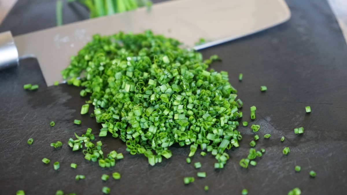 Ciboulette ciselée sur planche noire et couteau.