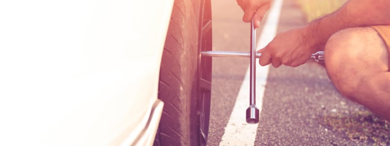 Homme changeant un pneu à l'aide d'une clé en croix