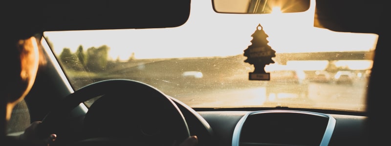 Achsvermessung und Spureinstellung bei einem Ford durchführen lassen und die Anzeichen und Kosten kennen Auto fährt auf der Autobahn der Sonne entgegegen mit Fokus auf Duftbaum, das an der Frontscheibe hängt