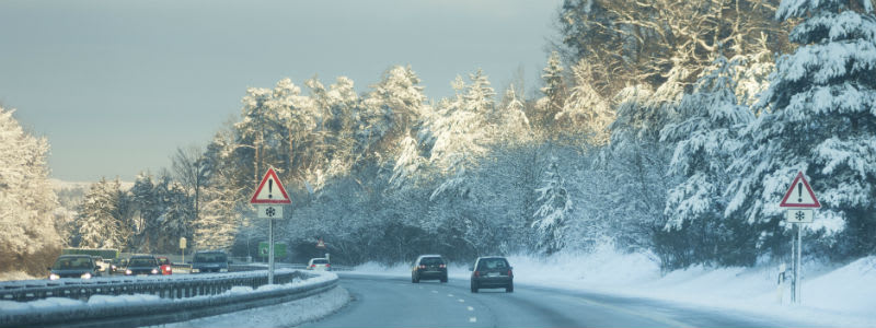 Bil på vej med sne og et skilt med advarsel om glatføre