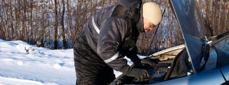 Bil gået i stå i vinterkulden Mand tjekker motor på bil i sneen