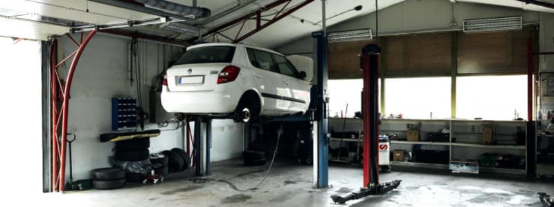 Autoværksted med bil på lift Hvid bil på værkstedet