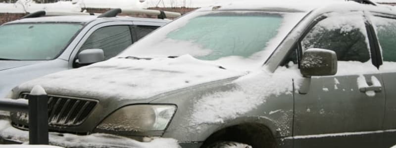 Snedækket bil på parkeringsplads Grå bil med pletvis sne