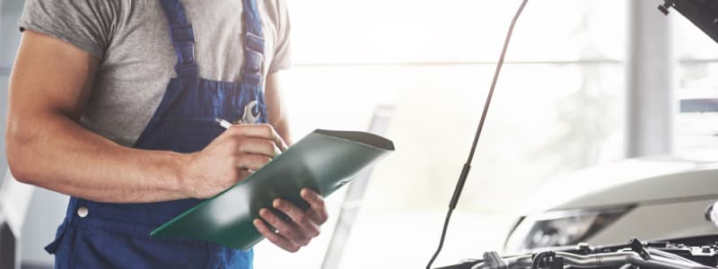 Comment se préparer à la révision de sa voiture Mécanicien vérifiant le moteur d'une voiture