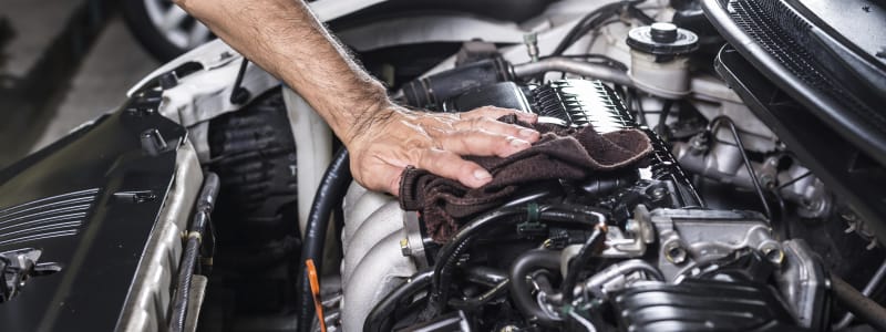 Ce qu'il faut savoir avant de laver le moteur de sa voiture Homme nettoyant un moteur de voiture
