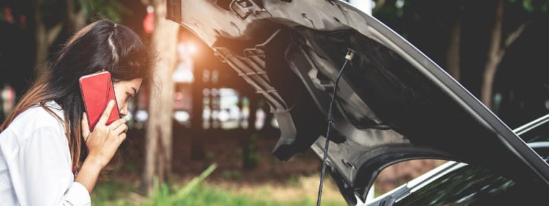 Ma voiture ne veux plus démarrer : quelles solutions ? Jeune femme brune au téléphone regardant sous le capot de sa voiture