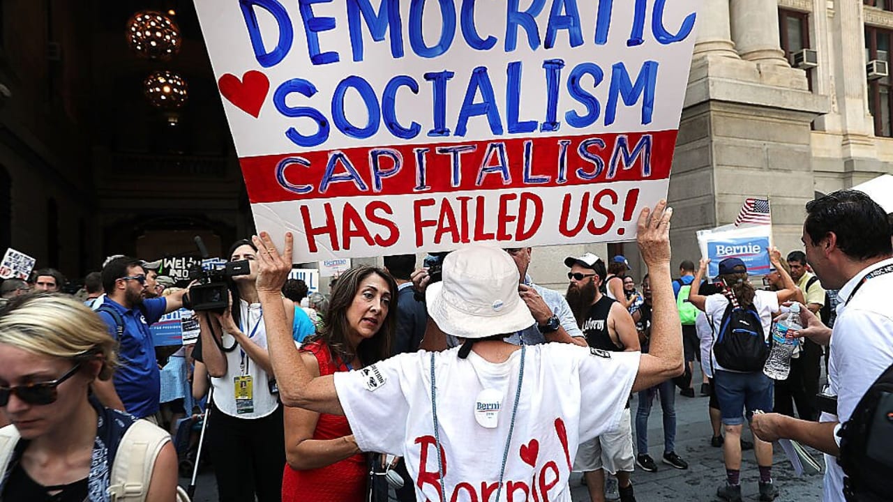 A person holding a sign that says "DEMOCRATIC SOCIALISM" and below "CAPITALISM HAS FAILED US!"