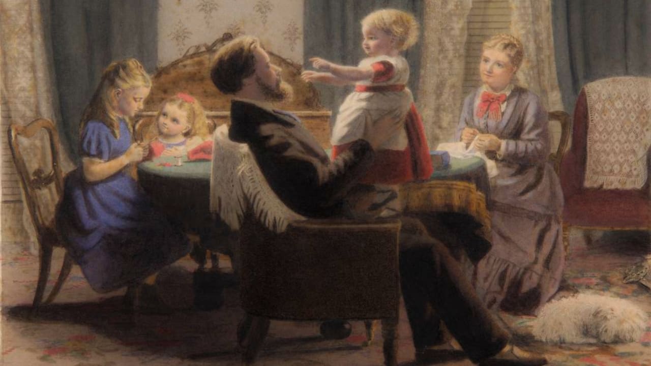 A family sits around a table. A child sits in her father's lap, arms outstretched.