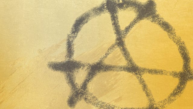 Anarchism "A" symbol overlaid on a gold background.