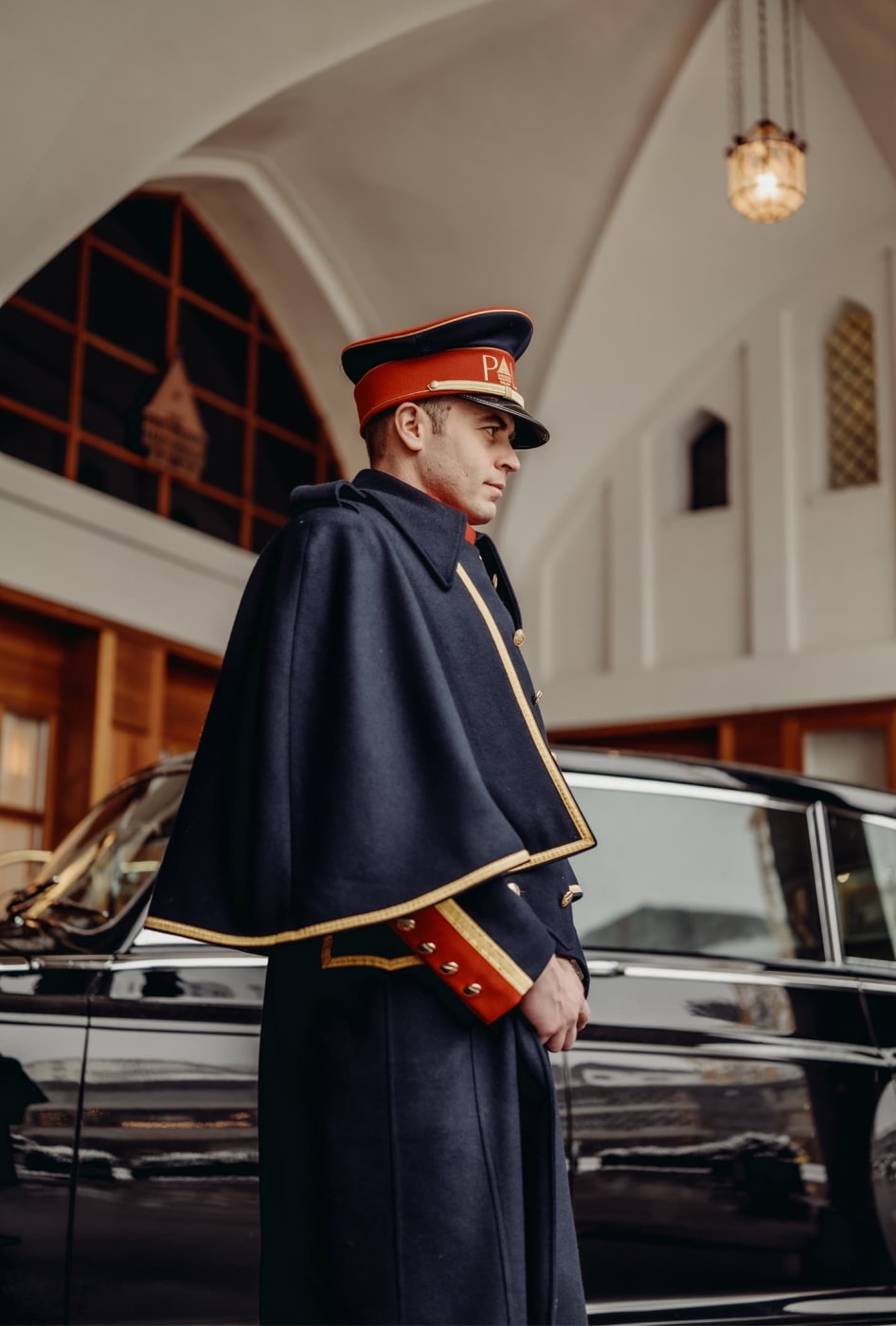 Ein Portier in Livree und Umhang neben einem Rolls-Royce am Eingang des Badrutt's Palace in St. Moritz