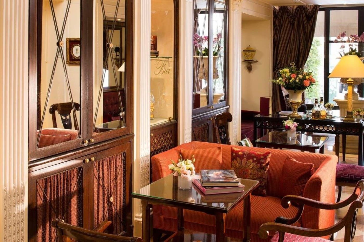 The lounge at Hôtel des Grands Hommes in Paris, with an orange sofa, wooden display cabinets and period armchairs