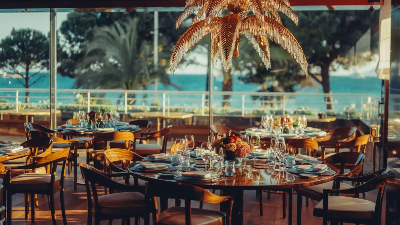 La salle du restaurant La Palme d'Or de l'Hôtel Martinez, lustre en palmier doré et vue sur la baie de Cannes