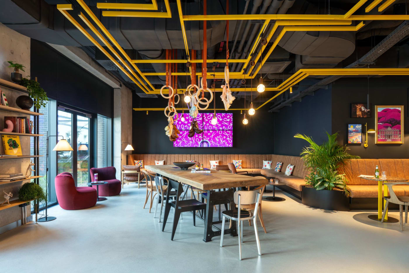 The communal table in the lobby of Moxy Budapest Downtown, beneath gymnastic rings and yellow pipes