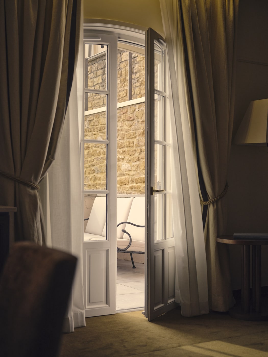 Une porte-fenêtre ouverte sur une terrasse aux murs de pierre, dans une chambre de la Villa Florentine