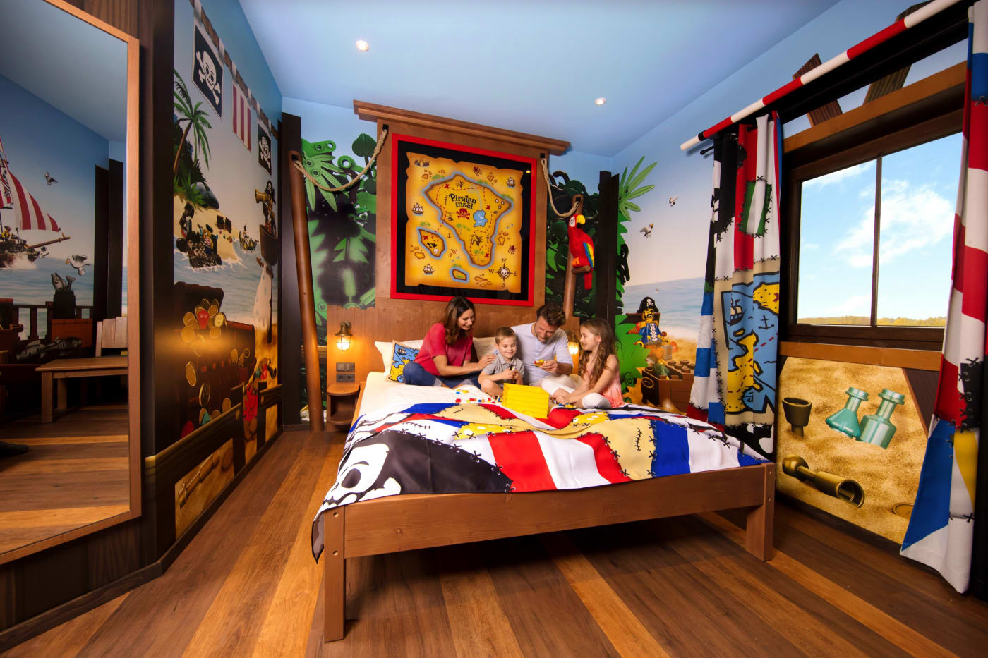 Family on the bed of a Pirateninsel Hotel room, with ship's cabin decor and a treasure map