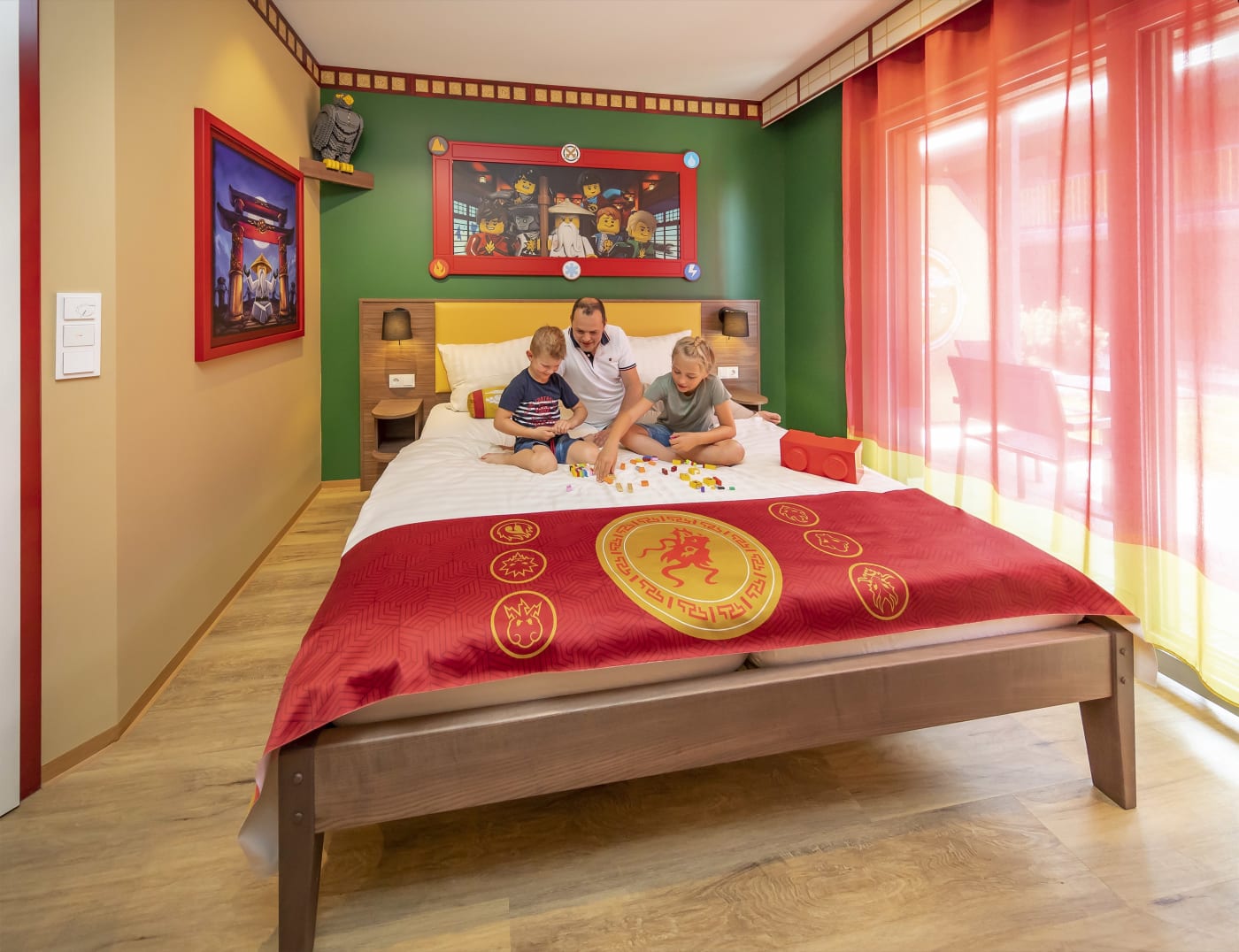 Father and children building LEGO on the bed of a NINJAGO Quartier room