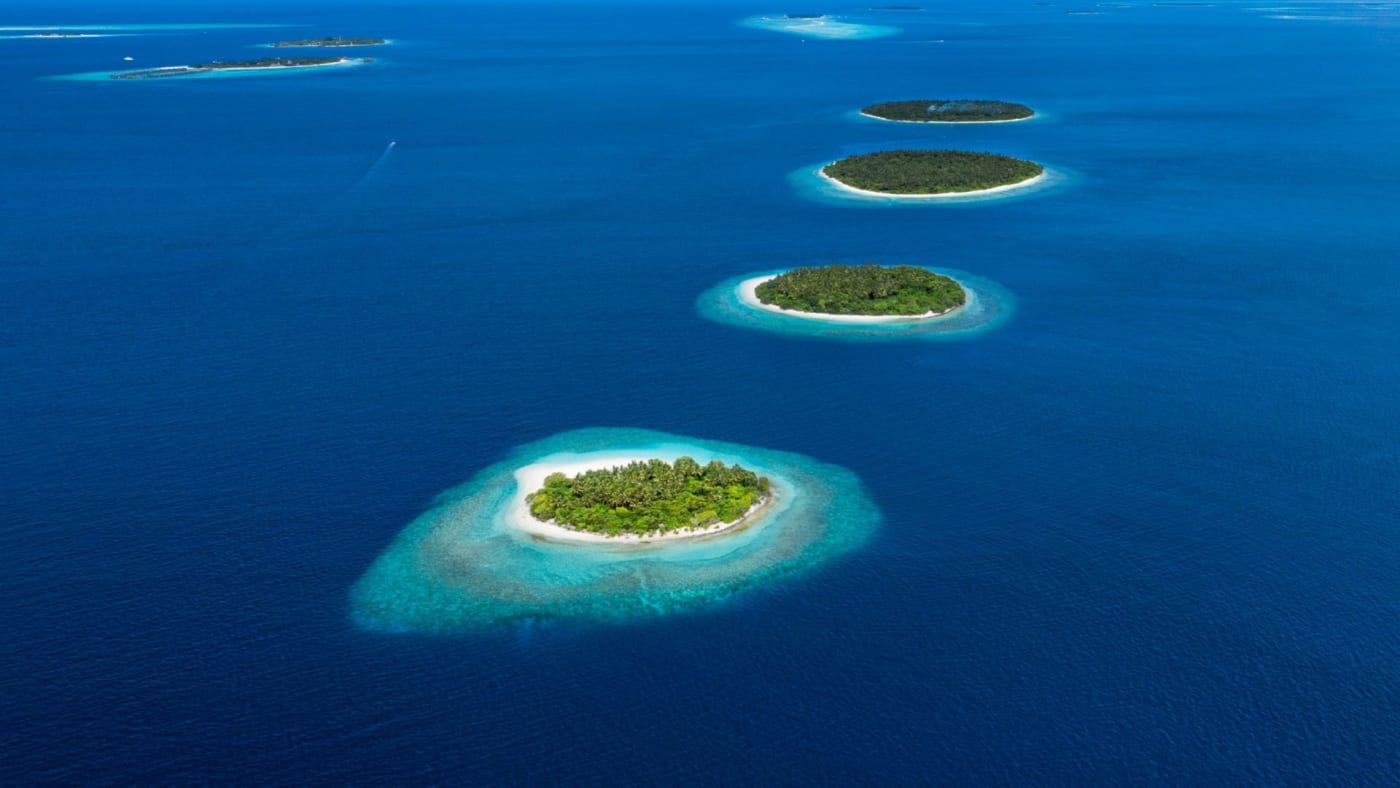 Vue aérienne d'un chapelet de petites îles vertes cerclées de lagons turquoise aux Maldives
