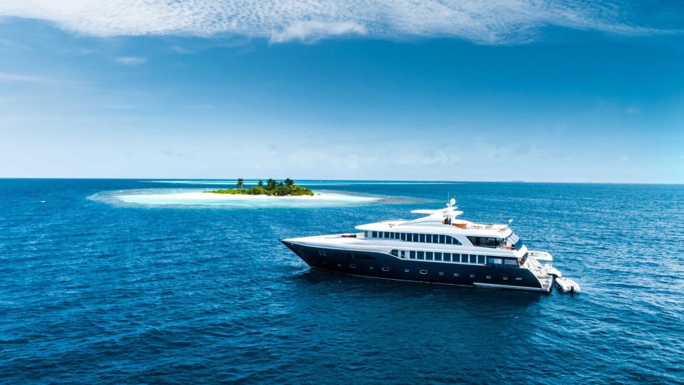 Un yacht blanc navigue près d'une petite île de sable aux Maldives