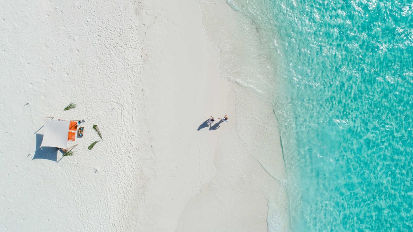 Vue du ciel d'une plage de sable blanc et d'une eau turquoise aux Maldives, avec un couple et un pique-nique