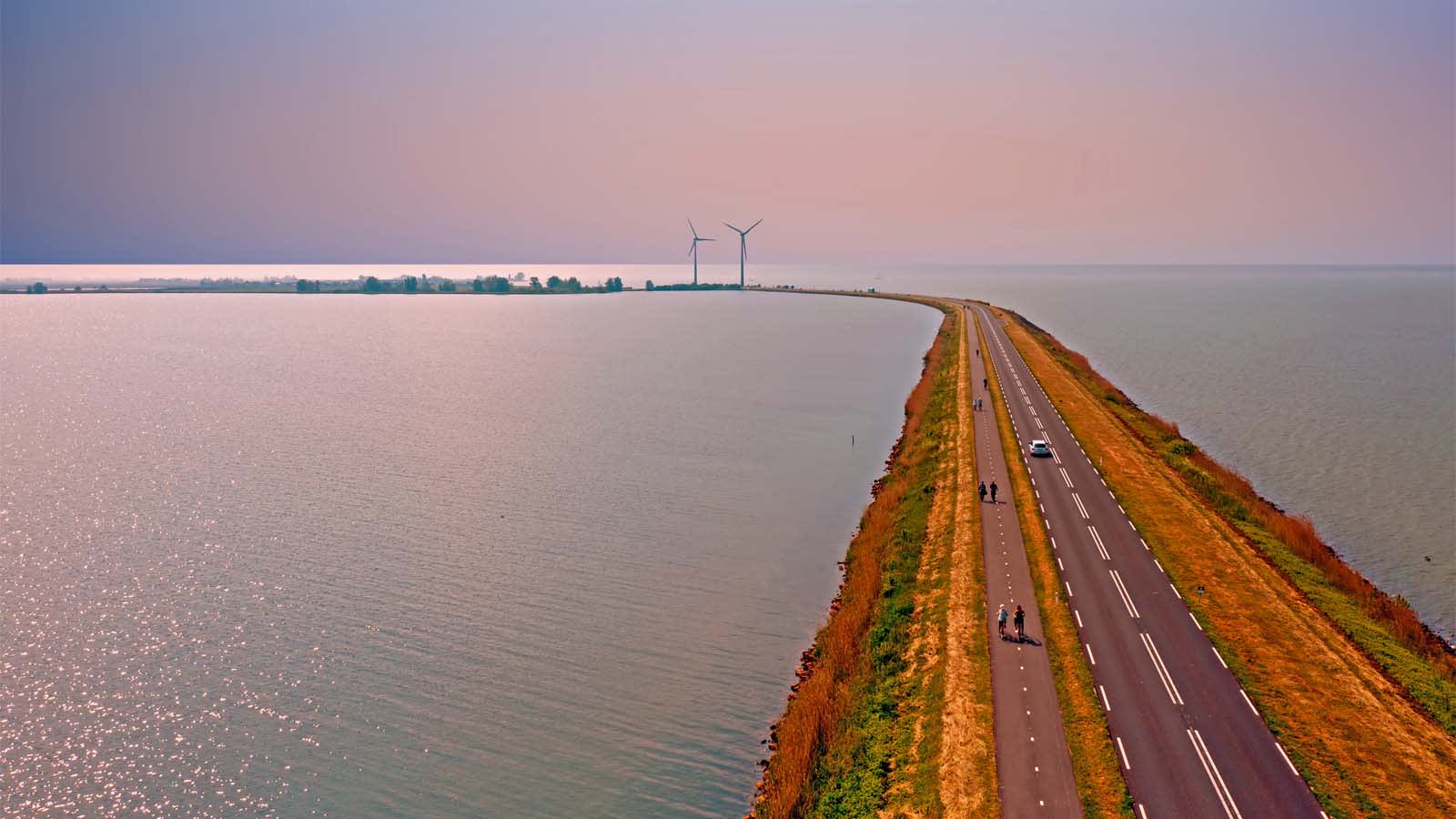 Wind turbines beside a coastal road at sunset