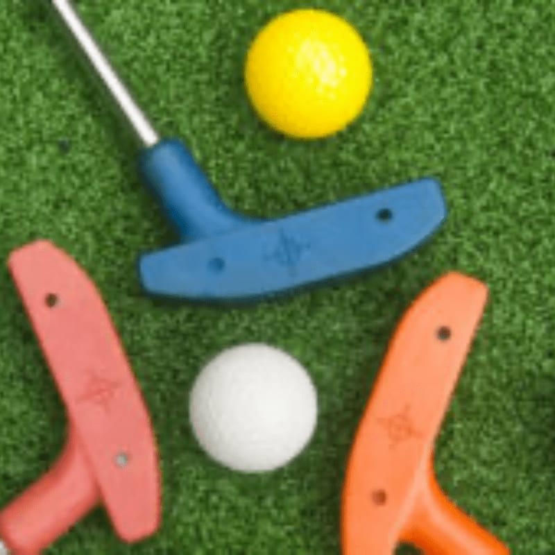 Three colorful putters and two golf balls rest on a green, artificial turf surface.