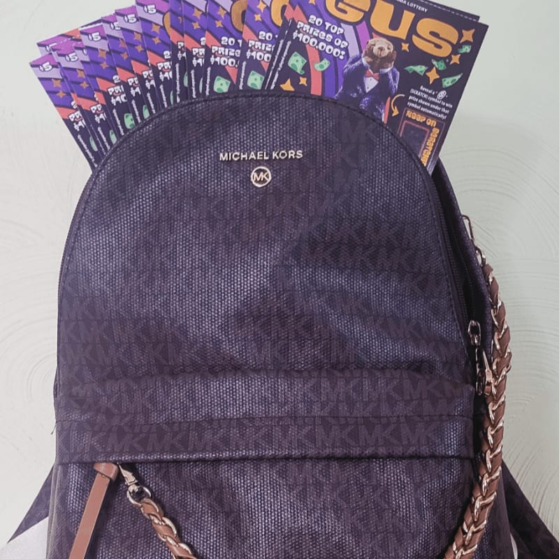 A dark purple Michael Kors backpack with lottery tickets sticking out of it sits against a light-colored wall.