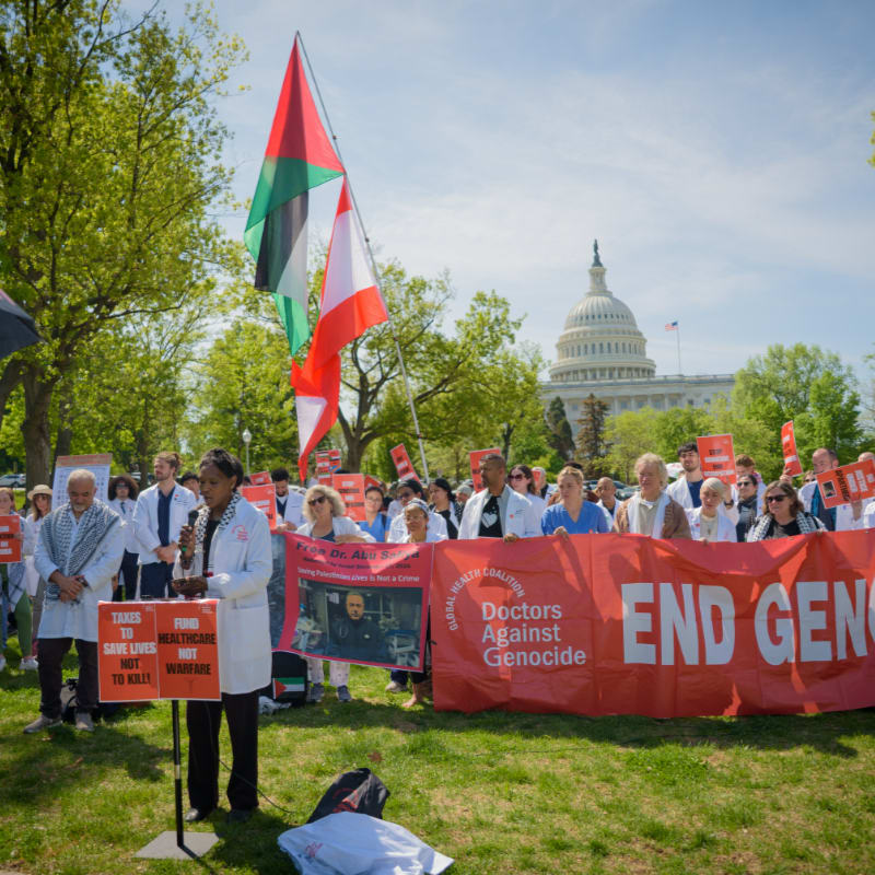 A group of people in white coats protest with signs and flags in front of the U.S. Capitol building.