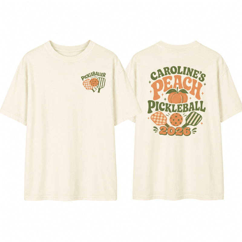 A cream-colored t-shirt is displayed with a small pickleball graphic on the left chest and a larger, colorful graphic on the back featuring a peach, pickleballs, and the text "CAROLINE'S PEACH PICKLEBALL 2026."